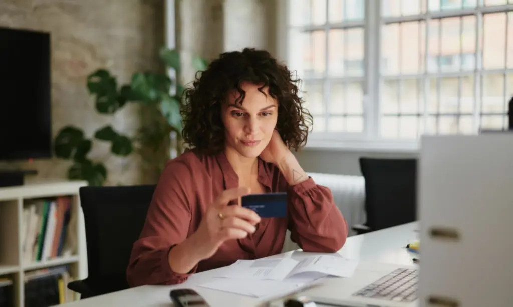 una mujer ante el ordenador, tiene una tarjeta de credito en la mano que utiliza para comprar
